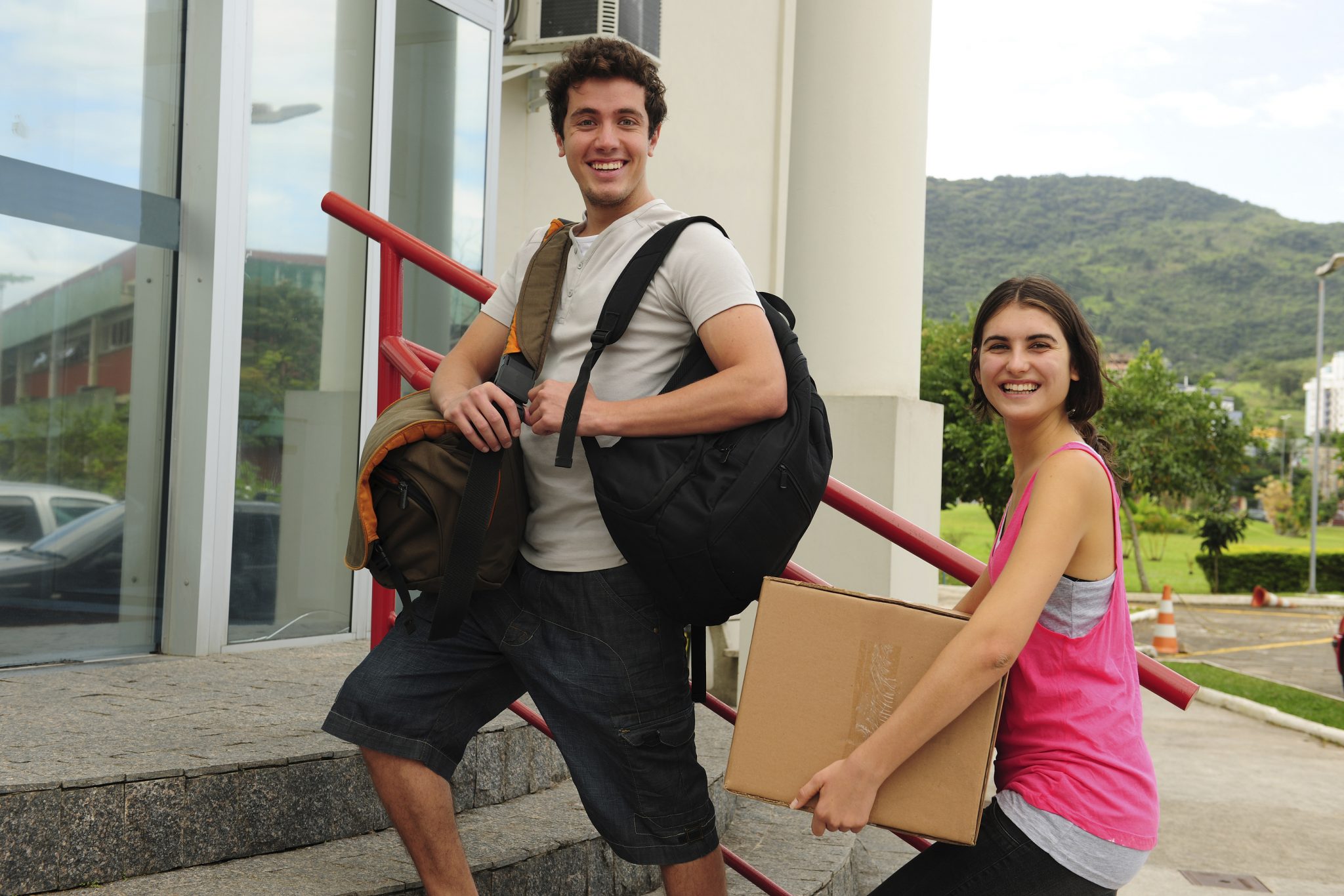 Zwei Studierende mit Rucksack und Umzugskarton auf einer Treppe