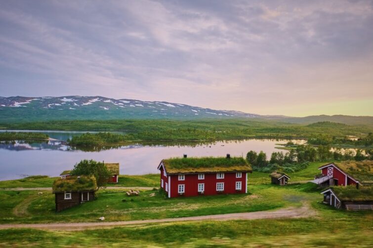 Entdecke das malerische Schweden! Dieses Bild zeigt idyllische rote Häuser vor einer atemberaubenden Kulisse aus Bergen und einem See, perfekt für alle, die das Auswandern nach Schweden in Erwägung ziehen. Ideal, um die Ruhe und Schönheit der schwedischen Landschaft zu genießen.