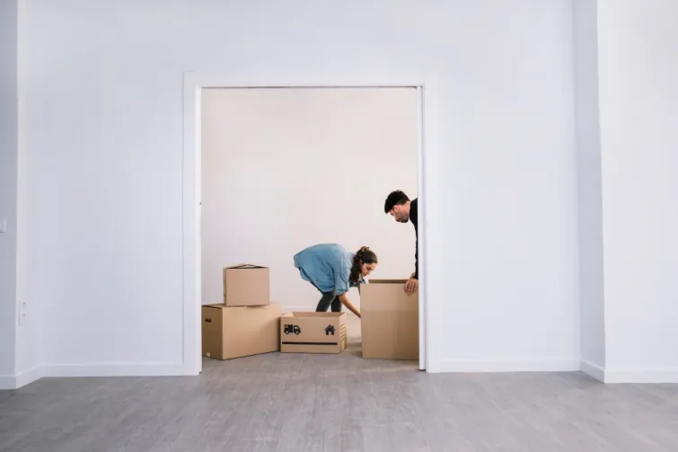 Ein junges Paar beim Einzug in ihr neues Zuhause, ausgestattet mit Umzugskartons in einem hellen, modernen Raum. Diese Szene zeigt die Aufregung und das gemeinsame Arbeiten, die mit einem Umzug verbunden sind.