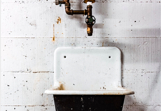 Altes Waschbecken mit Wasserhahn an einer Backsteinwand