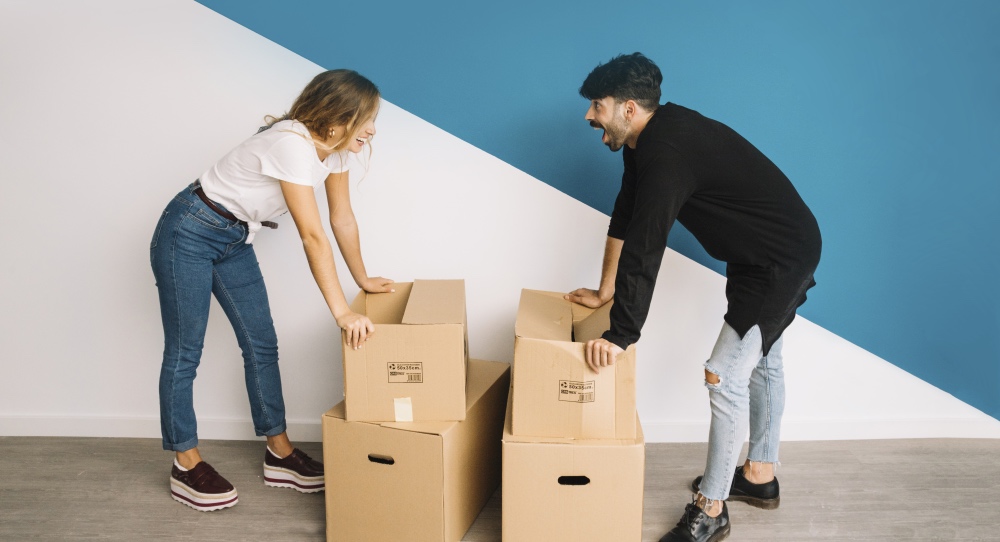 Pärchen lacht beim einpacken Umzugskartons weil sie Zeit gespart haben beim Umzug